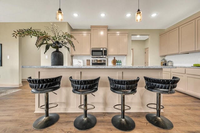 kitchen featuring decorative light fixtures, a kitchen bar, light wood-type flooring, and appliances with stainless steel finishes