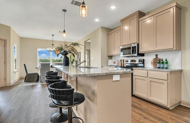 kitchen featuring sink, hardwood / wood-style flooring, an island with sink, appliances with stainless steel finishes, and decorative light fixtures