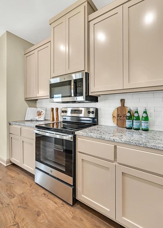 kitchen featuring light stone countertops, light hardwood / wood-style floors, cream cabinetry, decorative backsplash, and appliances with stainless steel finishes