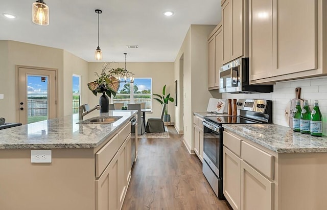 kitchen featuring appliances with stainless steel finishes, a kitchen island with sink, sink, light hardwood / wood-style floors, and hanging light fixtures