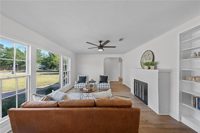 living room with hardwood / wood-style flooring, a brick fireplace, and ceiling fan