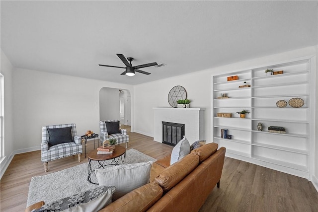 living room with wood-type flooring, a brick fireplace, and ceiling fan