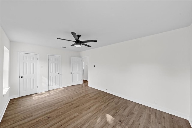 unfurnished bedroom featuring multiple closets, ceiling fan, and dark hardwood / wood-style floors