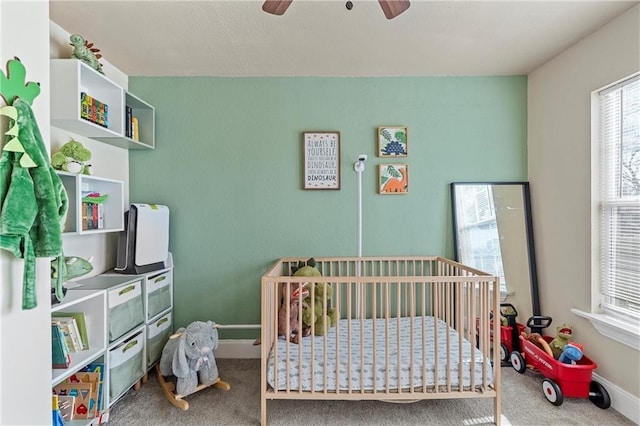 carpeted bedroom featuring ceiling fan and a nursery area