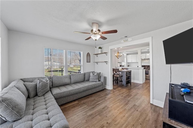 living room with ceiling fan with notable chandelier, hardwood / wood-style floors, and a textured ceiling