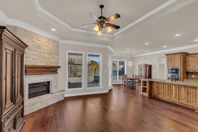 kitchen with light stone counters, ornamental molding, stainless steel appliances, dark wood-type flooring, and a stone fireplace