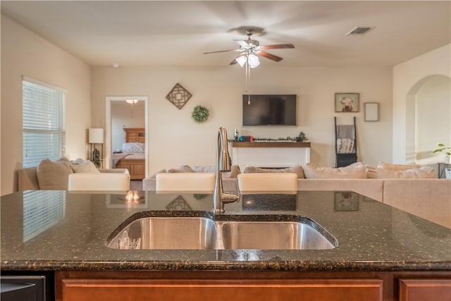 kitchen with ceiling fan, dark stone countertops, and sink