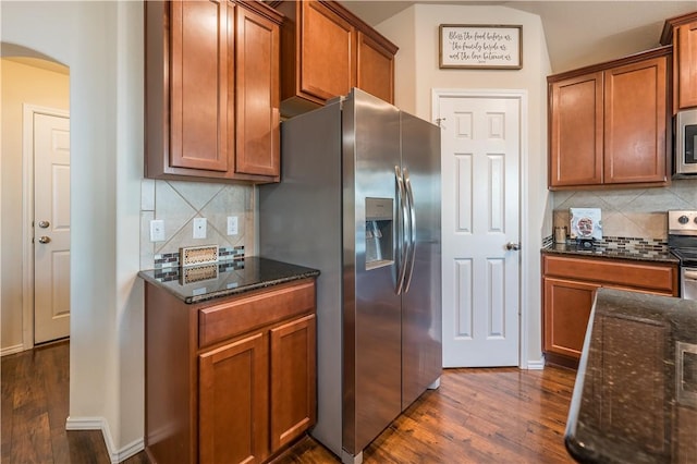 kitchen with dark hardwood / wood-style flooring, stainless steel appliances, dark stone counters, and tasteful backsplash