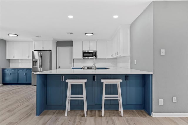 kitchen featuring light countertops, decorative backsplash, appliances with stainless steel finishes, a peninsula, and white cabinetry