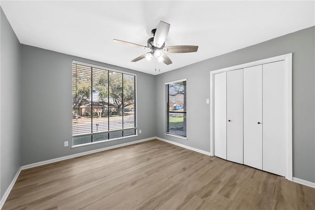 unfurnished bedroom featuring ceiling fan, a closet, baseboards, and wood finished floors