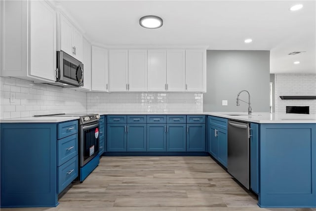 kitchen with a peninsula, blue cabinets, appliances with stainless steel finishes, and a sink