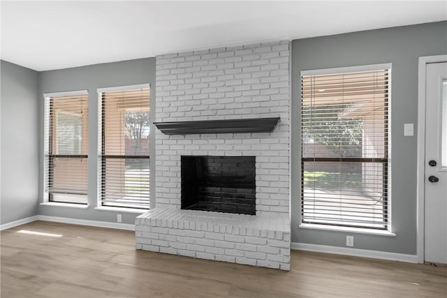 unfurnished living room with a brick fireplace, baseboards, and wood finished floors