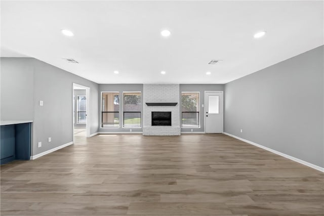 unfurnished living room featuring visible vents, wood finished floors, recessed lighting, baseboards, and a brick fireplace