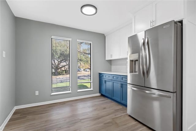 kitchen with light countertops, decorative backsplash, stainless steel fridge, white cabinetry, and blue cabinets