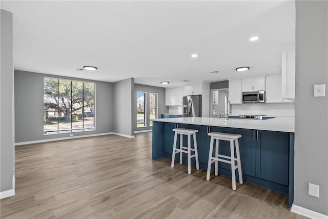 kitchen featuring baseboards, light wood-type flooring, light countertops, appliances with stainless steel finishes, and white cabinetry