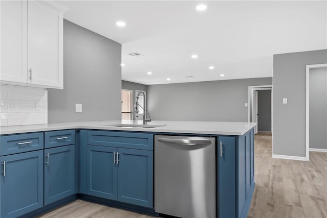 kitchen with light countertops, a peninsula, stainless steel dishwasher, blue cabinets, and a sink