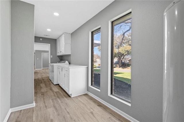 interior space featuring washer and dryer, light wood-style flooring, cabinet space, and baseboards