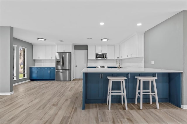 kitchen with a peninsula, a sink, stainless steel appliances, light countertops, and white cabinetry