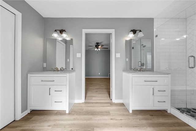 full bathroom with two vanities, wood finished floors, a stall shower, and a sink