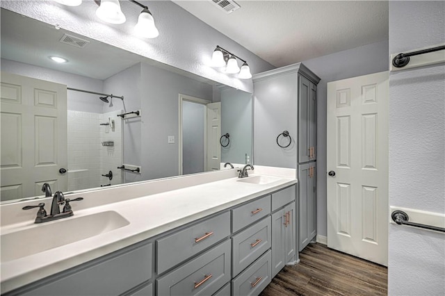 bathroom with hardwood / wood-style floors, vanity, tiled shower, and a textured ceiling