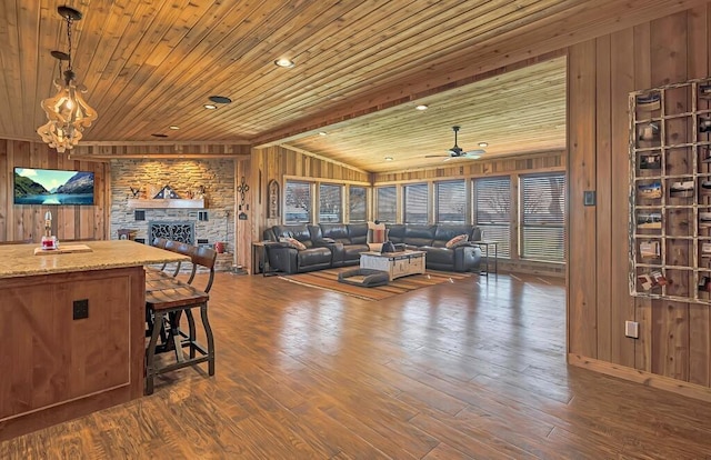 living room with a stone fireplace, dark hardwood / wood-style floors, wooden walls, ceiling fan, and wooden ceiling