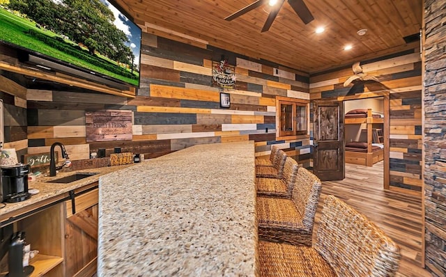 kitchen featuring wooden walls, sink, ceiling fan, light stone counters, and wooden ceiling