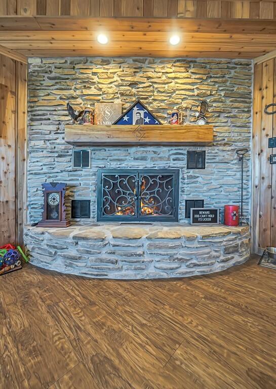 unfurnished living room with a fireplace, wood ceiling, wooden walls, and wood-type flooring