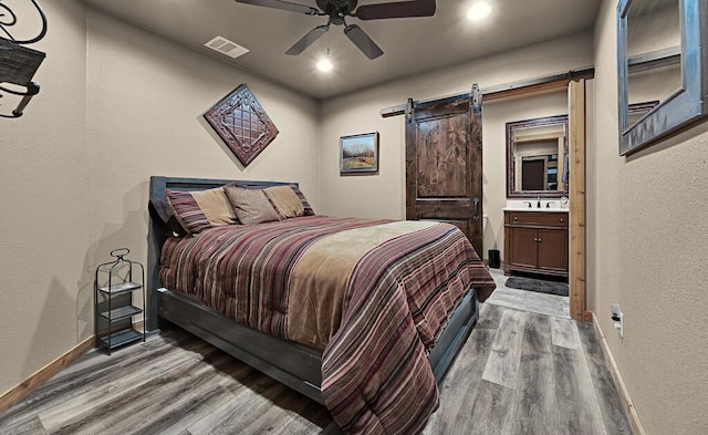 bedroom featuring hardwood / wood-style flooring, a barn door, connected bathroom, and ceiling fan