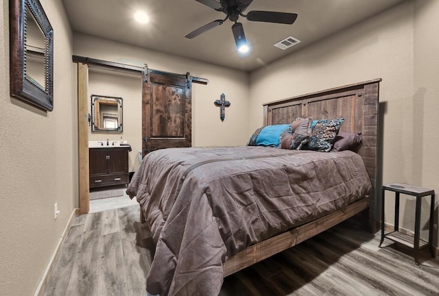 bedroom featuring connected bathroom, sink, ceiling fan, a barn door, and light wood-type flooring