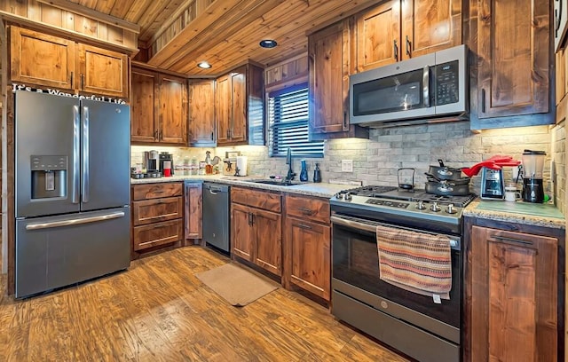 kitchen with sink, wood ceiling, appliances with stainless steel finishes, hardwood / wood-style flooring, and light stone countertops