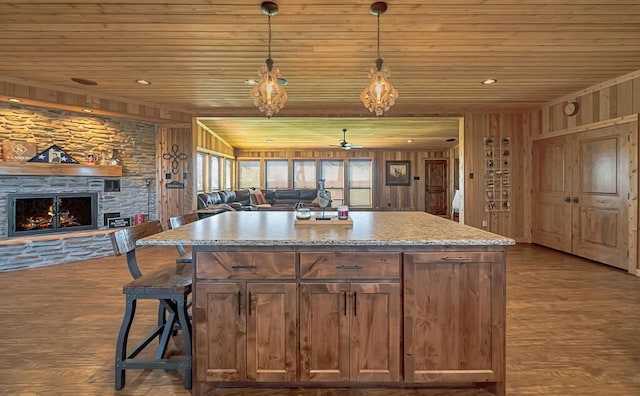 kitchen with decorative light fixtures, wooden walls, a stone fireplace, and wood-type flooring