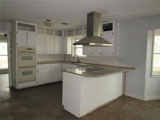 kitchen featuring kitchen peninsula, sink, white cabinetry, white double oven, and island exhaust hood