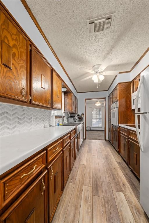 kitchen featuring a textured ceiling, decorative backsplash, white appliances, and light wood-type flooring