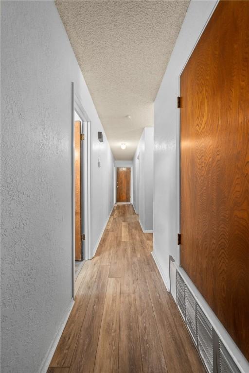 hall with light hardwood / wood-style flooring and a textured ceiling