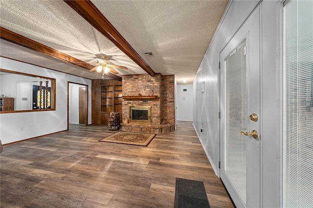 unfurnished living room featuring a brick fireplace, a textured ceiling, wood-type flooring, built in features, and beamed ceiling