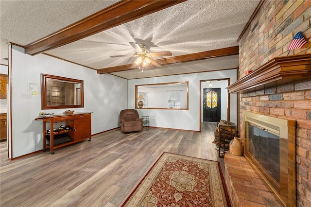 living area featuring beam ceiling, ceiling fan, wood-type flooring, a textured ceiling, and a fireplace