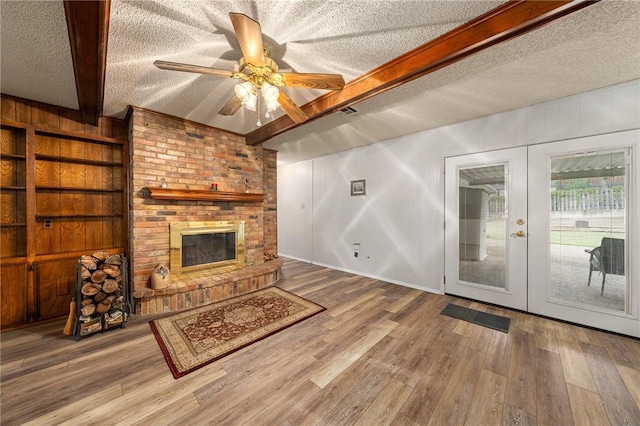 living room with french doors, a textured ceiling, beamed ceiling, a fireplace, and hardwood / wood-style floors