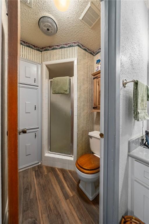 bathroom featuring hardwood / wood-style floors, a textured ceiling, toilet, vanity, and a shower with shower door