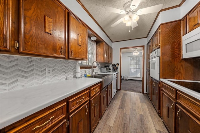 kitchen featuring sink, a textured ceiling, white appliances, decorative backsplash, and light wood-type flooring