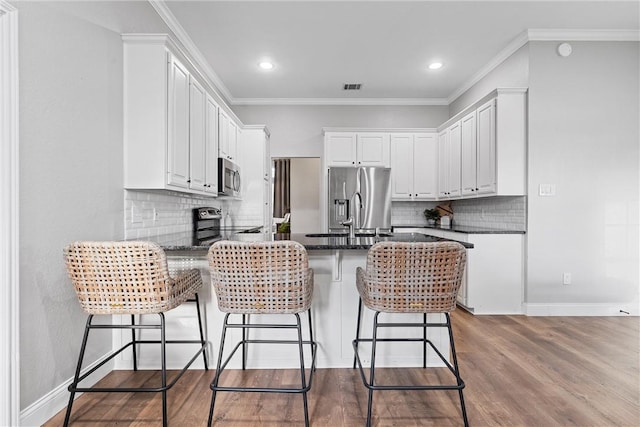 kitchen with ornamental molding, appliances with stainless steel finishes, kitchen peninsula, hardwood / wood-style floors, and white cabinets