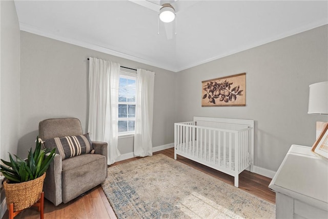 bedroom featuring crown molding, hardwood / wood-style flooring, a crib, and ceiling fan