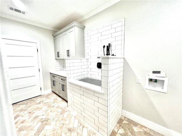 kitchen with gray cabinetry, crown molding, decorative backsplash, and light wood-type flooring