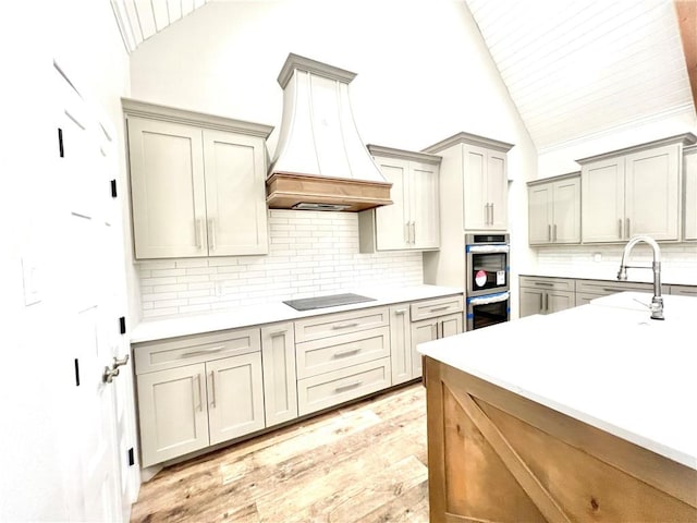 kitchen featuring black electric stovetop, vaulted ceiling, double oven, and custom exhaust hood