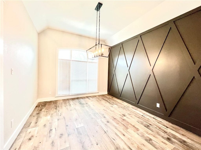 unfurnished dining area with a notable chandelier, light wood-type flooring, and vaulted ceiling