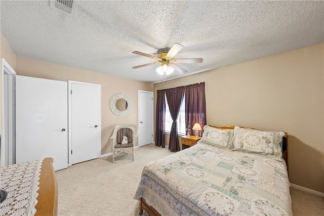 bedroom with ceiling fan, two closets, light colored carpet, and a textured ceiling