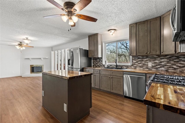 kitchen featuring sink, a brick fireplace, appliances with stainless steel finishes, a kitchen island, and hardwood / wood-style flooring