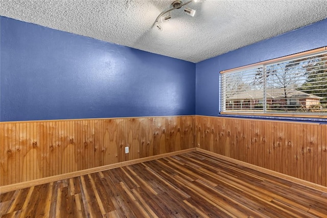 spare room with wood-type flooring, wooden walls, and a textured ceiling