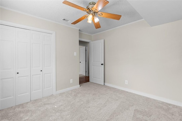 unfurnished bedroom with crown molding, a closet, light carpet, and a textured ceiling