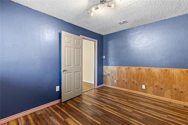 unfurnished room with wooden walls, a textured ceiling, and dark hardwood / wood-style flooring