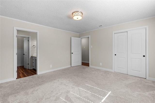 unfurnished bedroom with dark colored carpet, ornamental molding, a textured ceiling, and a closet